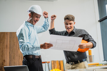 Wall Mural - A Caucasian middle-aged male engineer contractor and an Italian architect engineer are seated at a desk, discussing renovation plans with blueprints and a house model in front of them.