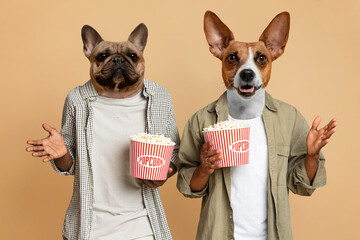 Two dogs wearing human clothing are holding buckets of popcorn in their hands. The dogs are both looking at the camera with surprised expressions on their faces.