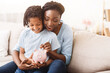 © Prostock-studio - Money Saving Concept. Excited black mom and daughter putting coins into piggy bank, free space