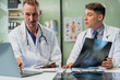 © NanSan - Caucasian middle-aged male doctor and Italian scientific researcher are seated at desk, discussing innovative antiviral drug inventions, with a monitor displaying the latest technology advancements.