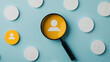 © tonstock - Magnifying glass highlighting a user icon among many others on a light blue background, symbolizing focus, research, and individual search.