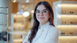 © leszekglasner - Smiling female optometrist standing confidently in a modern glasses store, showcasing professional service and eyewear options.