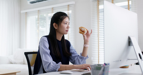 Asia people young woman MBA student gen Z girl work online on desk at home office multi tasking workforce hurry eat junk meal break time bite vegan meat burger diet. Stress relief by take out food.