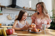 © Dmytro Hai - Smiling woman giving pastry to daughter in kitchen at home
