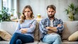 © Four888 - Frustrated partners sit apart on a couch, faces stern, arms crossed, and eyes averted, surrounded by a blurred, isolated background, exuding tension and discord.