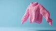 © Nadin Faust - 3D render of a pink sweater floating in the air against a blue background, featuring detailed hand-knitted texture in a studio shot