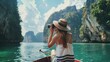 © VK Studio - A hat-wearing woman photographs stunning cliffs from a boat in a tranquil, teal-colored lagoon under a vast, cloudy sky.