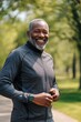 © Oscar - Smiling senior black man running in a park wearing sportswear and a smartwatch