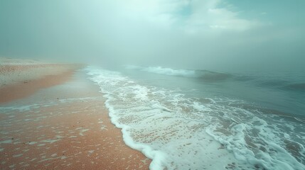 Wall Mural - Foggy shoreline with gentle waves rolling onto sandy beach during early morning light