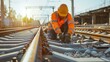 © VK Studio - A construction worker in safety gear performs maintenance on rail tracks under the warm glow of the early morning sun.