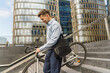 © muse studio - A professional man in business attire carries his bicycle up a set of stairs in a modern urban environment.