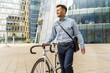 © muse studio - A professional man in business attire walks with his bicycle in a modern urban setting, embodying an active and balanced lifestyle.