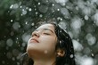 © Victor Bertrand - A woman with closed eyes enjoys a serene moment in the rain as water droplets cascade around her, shimmering against a blurred green background.