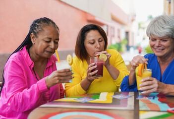 Happy multiracial senior women meeting in the city while drinking smoothie at bar terrace - Joyful elderly female friends concept