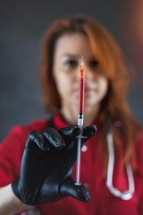 female doctor wearing red uniform medical gloves holding a syringe with blood isolatedon black