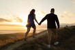 © KONSTANTIN SHISHKIN - Loving couple holding hands and walking up a hill at sunset