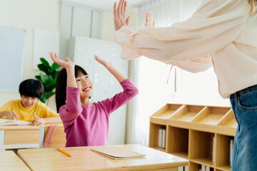 Joyful Asian primary student celebrating achievement with teacher through energetic high-five