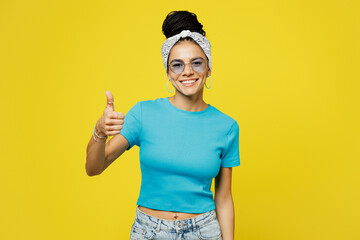 Wall Mural - Young smiling happy cheerful Latin woman she wear blue top t-shirt headband glasses casual clothes showing thumb up like gesture isolated on plain yellow background studio portrait. Lifestyle concept