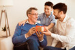 © Prostock-studio - Mature Father And Son Congratulating Grandpa Giving Him Birthday Gift Sitting On Sofa At Home. Selective Focus