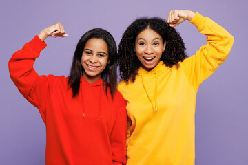 Wall Mural - Two young little kid teen girls women they wear red yellow hoodie casual clothes show biceps muscles on hand demonstrating strength power isolated on plain light purple background. Lifestyle concept.