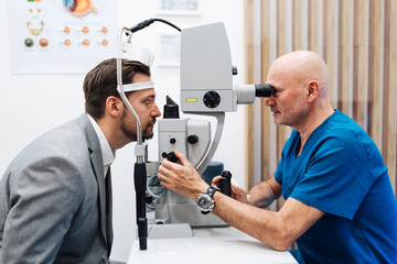 Attractive male doctor ophthalmologist is checking the eye vision of handsome middle age man in modern clinic. Doctor and patient during medical check up in ophthalmology clinic.