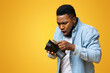 © Prostock-studio - Where's my money. Shocked african american guy holding wallet with dollar cash that will be not enough to cover spendings, yellow studio background.