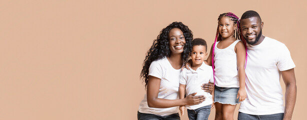 Wall Mural - Happy millennial family. Portrait of smiling african parents with their two little kids over yellow background