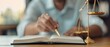 © Mikus - A person sits at a table, holding a book and pen, with a scales of justice in front of them