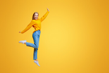 Wall Mural - Be yourself. Pretty young girl jumping in air and laughing on orange background, free space