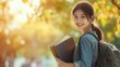 © Nathan - Smiling Asian female student with books in a sunny outdoor setting, exuding happiness and enthusiasm for learning.