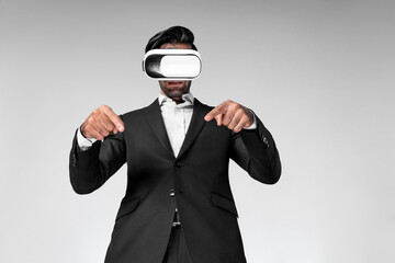 Smart business man wearing VR headset and suit while pointing at something. Caucasian investor connect mentaverse and virtual reality world while using VR goggles and standing. Innovation. Deviation.