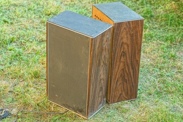 pair of big square powerful plastic black old electric acoustic music dirty retro simple industrial speakers standing on green grass during daytime outdoors