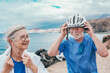 © luciano - Active senior couple of cyclists wearing helmets enjoying healthy lifestyle riding with electric bicycles in off road along the sea