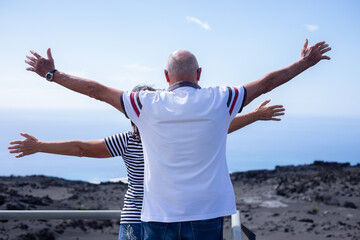 Canvas Print - Rear view of Senior Caucasian couple with outstretched arms looking at horizon over sea. Elderly retirees enjoying Vacation Travel and Freedom. Retirement Lifestyle Concept