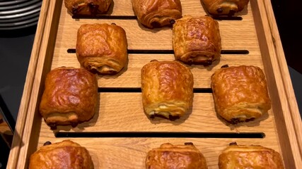 Wall Mural - Croissant chocolate on wooden tray displayed in breakfast selfservice, slider tracking shot on pain au chocolat