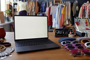 Close up on laptop with white blank screen on wooden table with second hand sunglasses and accessories at thrift shop, copy space