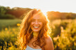 © MVProductions - Young happy smiling woman standing in a field with sun shining through her hair