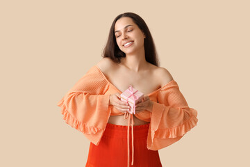 Wall Mural - Happy young woman with gift box on beige background