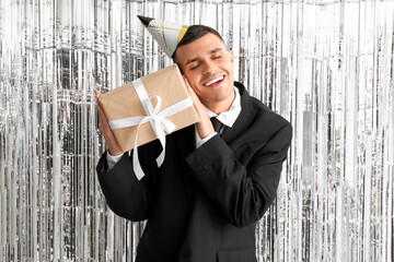 Wall Mural - Young man in party hat with gift box celebrating Birthday on tinsel background