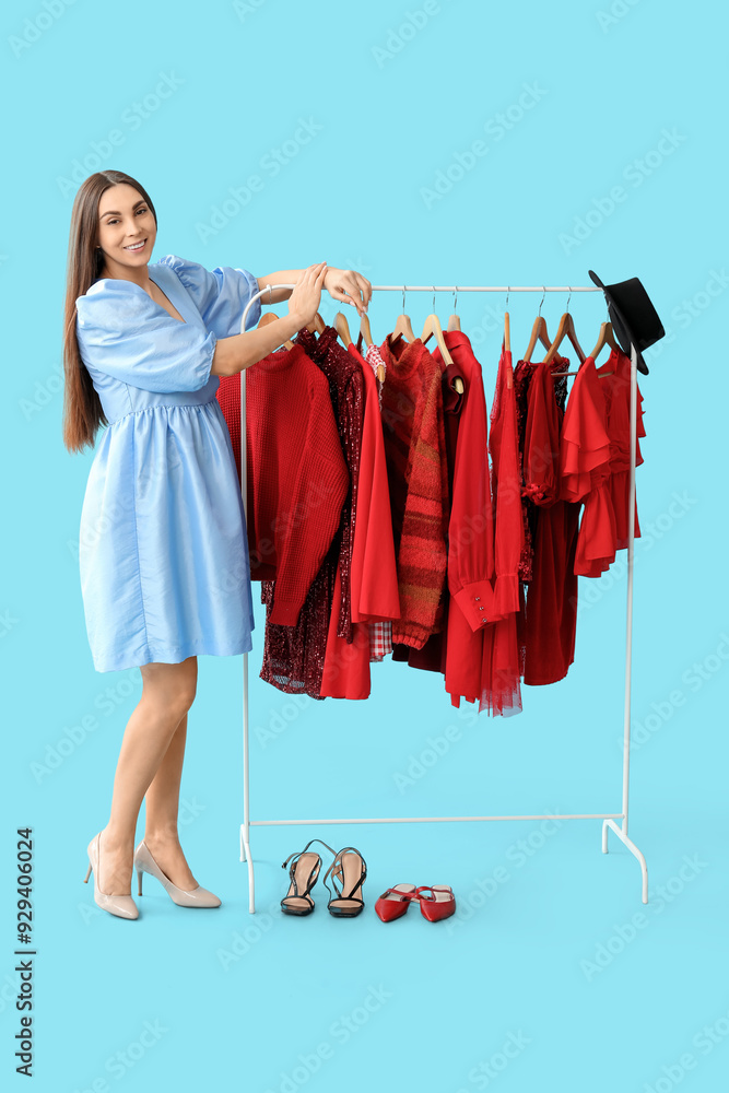 Happy female stylist with clothes on rack against blue background