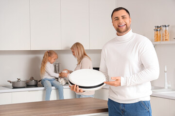 Poster - Happy father with robot vacuum cleaner and his family in kitchen