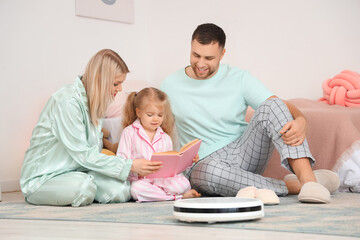 Poster - Happy family with robot vacuum cleaner reading book in children's bedroom