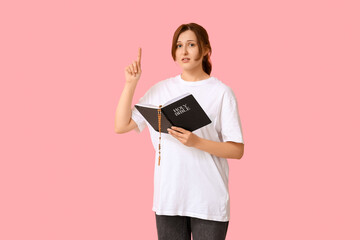 Wall Mural - Religious young woman with wooden cross pointing at something on pink background