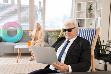 Poster - Mature businessman with laptop ready for summer vacation in office