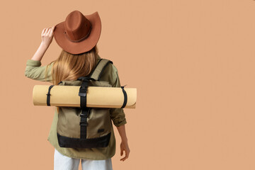 Wall Mural - Young woman with hat and backpack on beige background. Travel concept. Back view