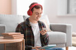 © Pixel-Shot - Young man listening to audiobook and using mobile phone in living room