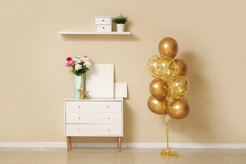 Poster - Beautiful golden air balloons with home decor and flowers on commode near beige wall at home