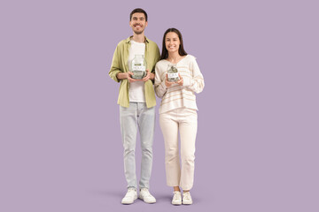 Wall Mural - Young couple with jars of money on lilac background