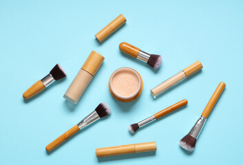 Wall Mural - Stylish makeup brushes with cosmetic products on blue background