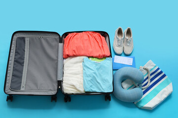 Poster - Travel pillow, wallet, ticket and suitcase with clothes on blue background